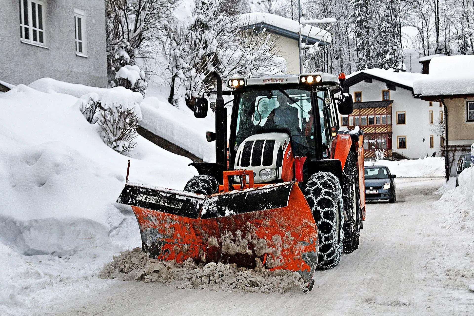 Ein Schneeräumungsfahrzeug mit einem orangefarbenen Schneepflug, der Schnee von einer Straße schiebt.